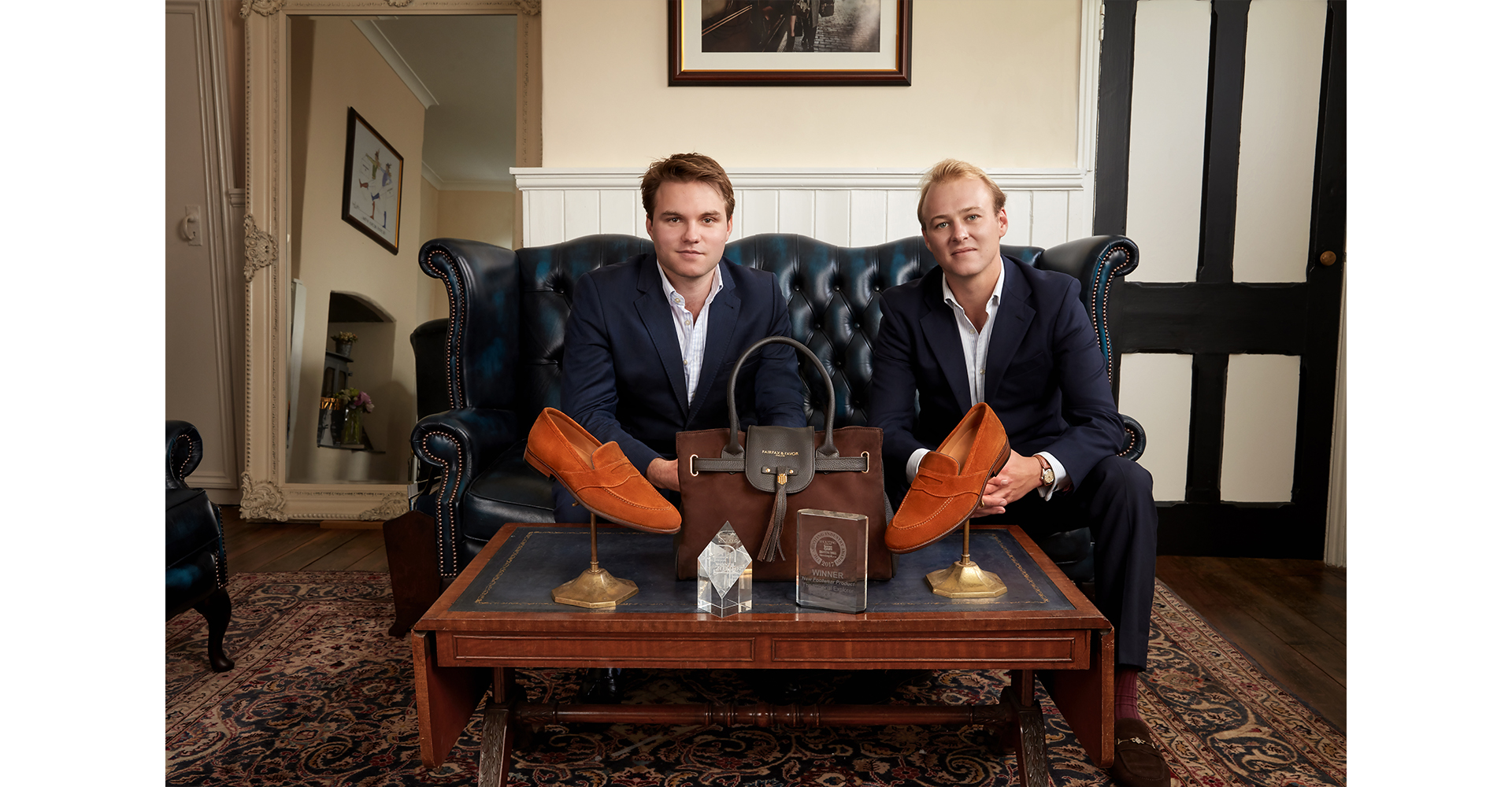 2 men sitting down table in front of them with shoes and handbag corporate head shot for the cofounders of Fairfax and Favor