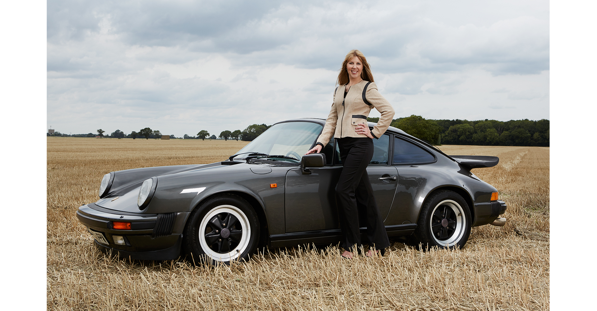 business woman standing in field in front of her Porshce 911 car corporate head shot
