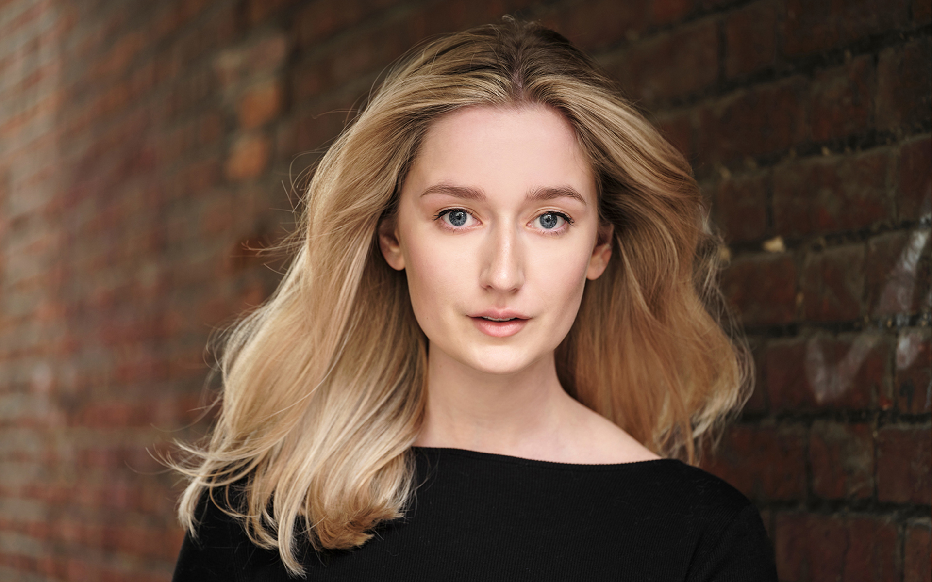 An actress having a head shot photographed in natural light front of a brick wall