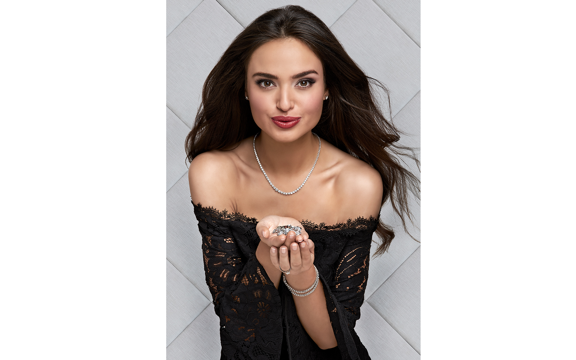 Model wearing jewellery  on a Winsor Bishop advertising photo shoot blowing diamonds front of a grey padded wall