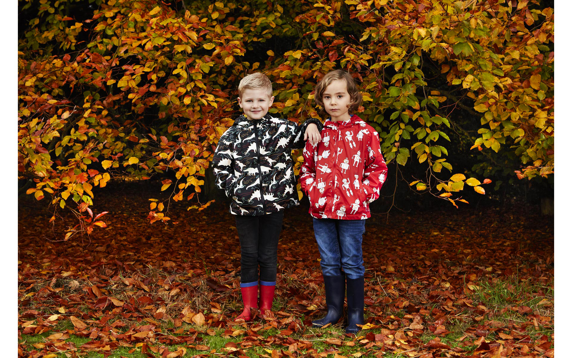 2 boy models wearing rain coats from of autumn trees and leaves on photo shoot