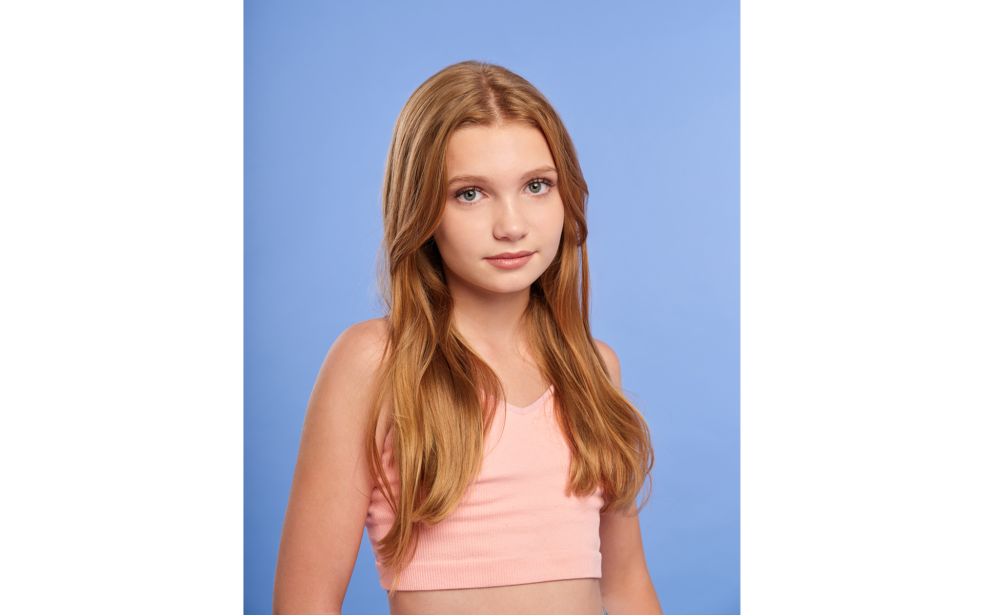 Blonde teenage model wearing pink top in front of blue back drop on a brand fashion photo shoot