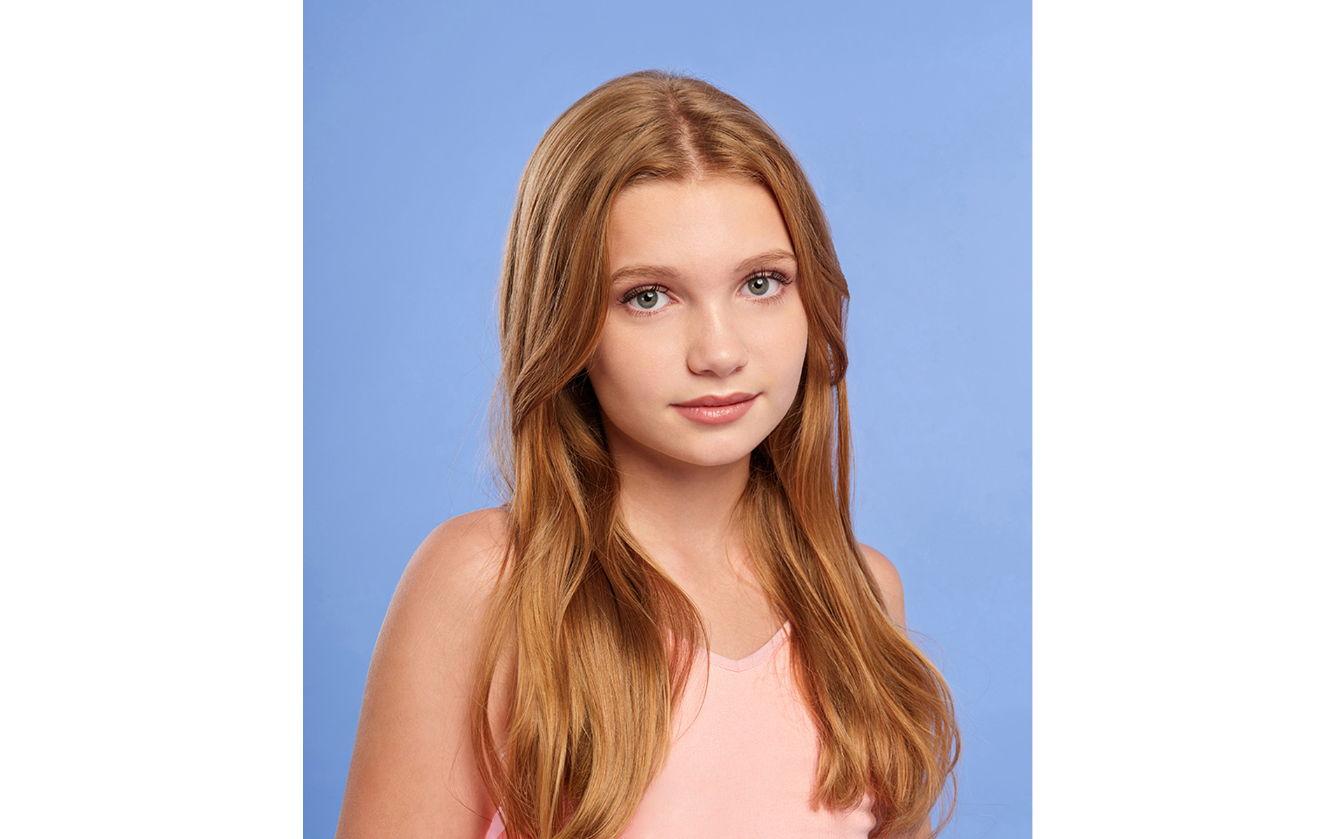 Blonde teenage model wearing pink top in front of blue back drop on a brand fashion photo shoot