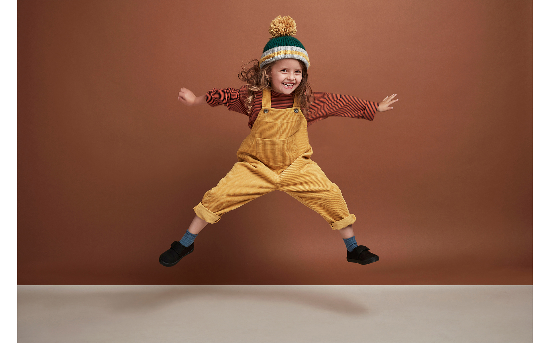 Young girl model jumping in the air front of brown back drop in children's  brand fashion photo shoot 