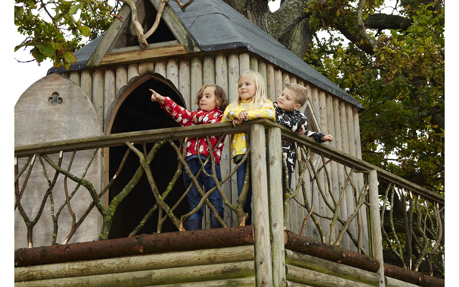 3 child models in rain coats in a wooden tree house in Norfolk country on a fashion photo shoot